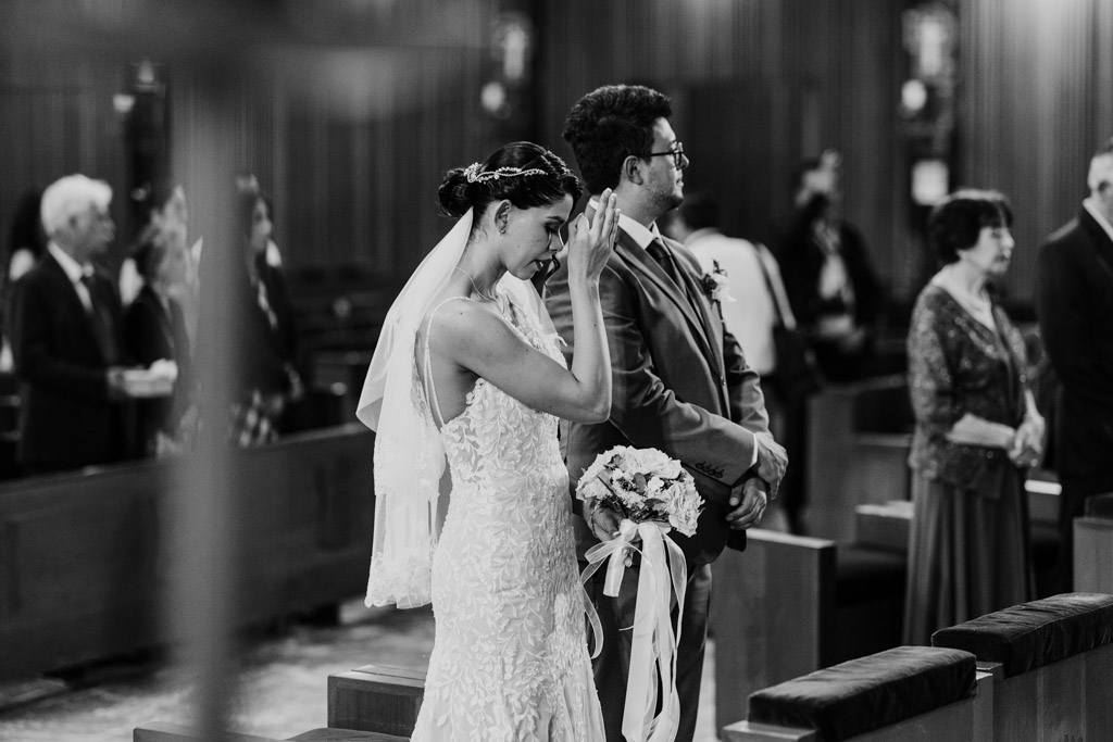 Black and white photo of bride wiping away tears as she stands beside the groom during her wedding ceremony at Parroquia San Cayetano in Mexico City