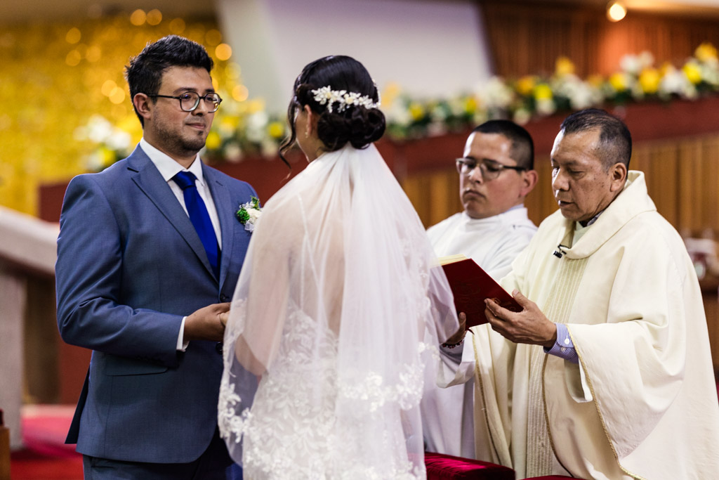 Priests speaks while bride and groom hold hands during wedding ceremony at Parroquia San Cayetano in Mexico City