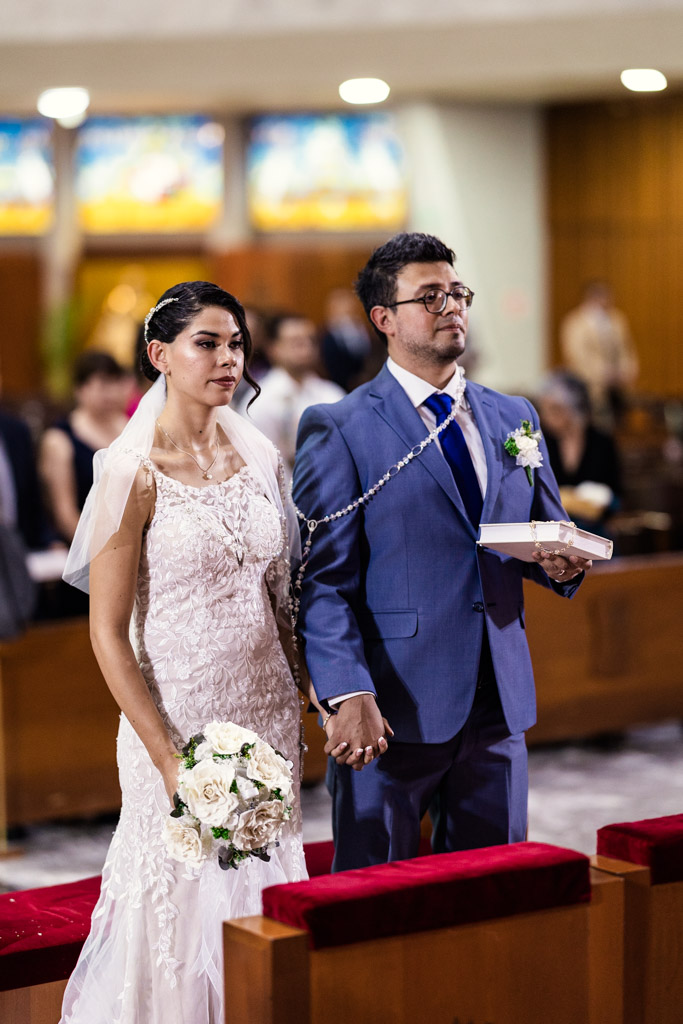 Bride and groom holding hands draped with a lasso during their wedding ceremony at Parroquia San Cayetano