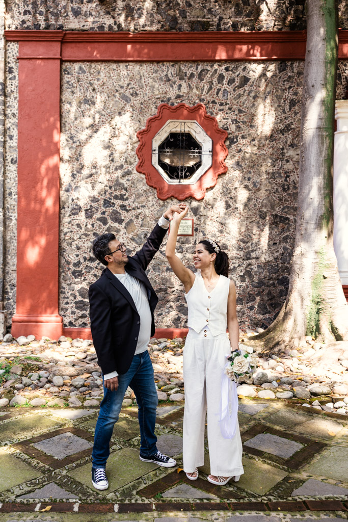 Newlywed couple dances outdoors in front of stone church wall with red accents