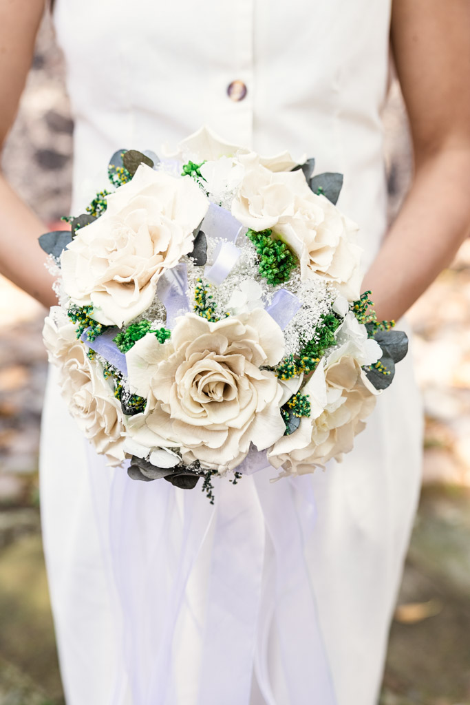 Detail photo of bride's bouquet of white roses with green accents and a white ribbon