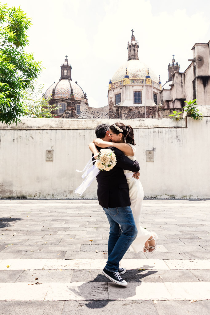Bride and groom embrace joyfully outdoors in the courtyard of Museo de El Carmen in San Angel neighborhood of Mexico City