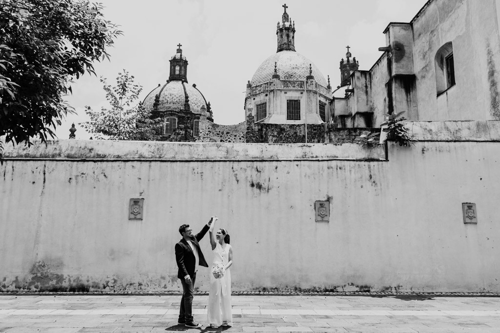 Black and white photo of newlywed couple dancing in the courtyard of Museo de El Carmen featureing the church's domes and tall stone courtyard wall