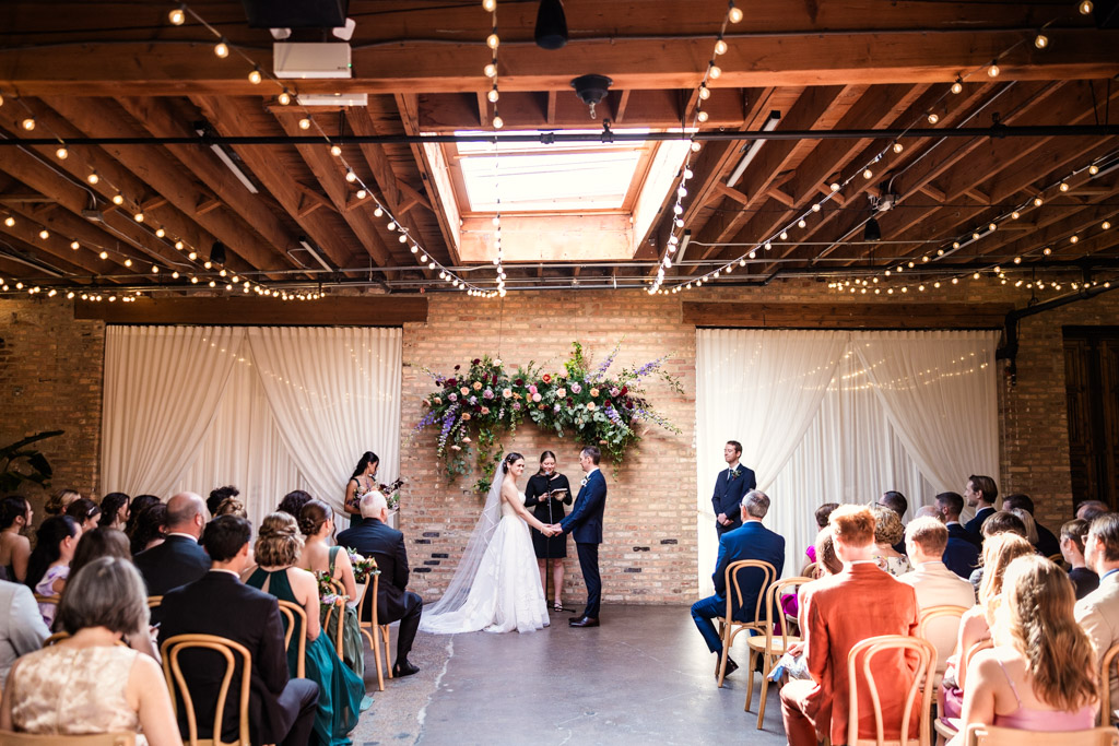 A couple stands holding hands during an wedding ceremony at The Arbory Chicago, with guests seated around them