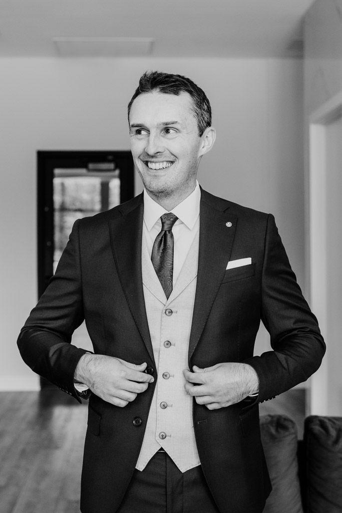 Black and white photo of groomn in a suit adjusting his jacket while getting ready for his Arbory Chicago wedding celebration