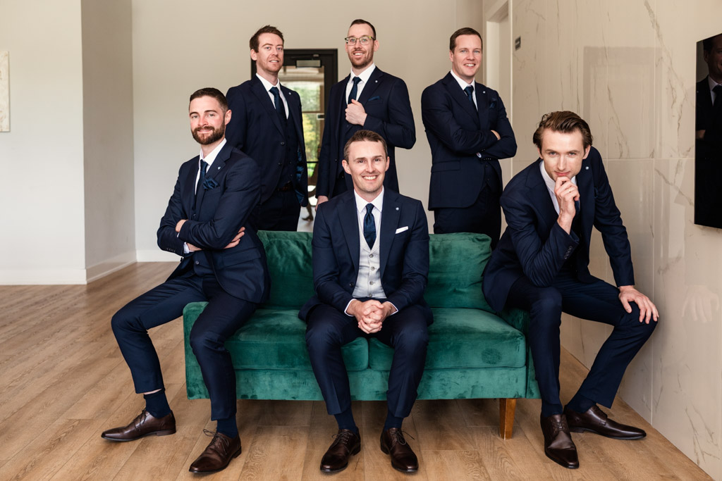 Groom and groomsmen in suits pose on a green couch before his wedding celebration at The Arbory Chicago