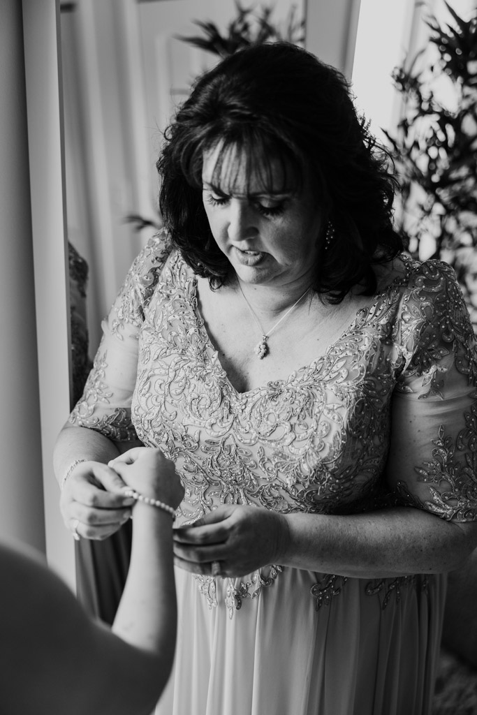 Black and white photo of bride's mother helping bride fasten a bracelet while getting ready for wedding celebration at The Arbory Chicago