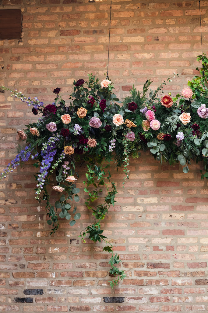 A lush floral arrangement with roses and greenery hangs on a brick wall.for a wedding celebration at The Arbory Chicago