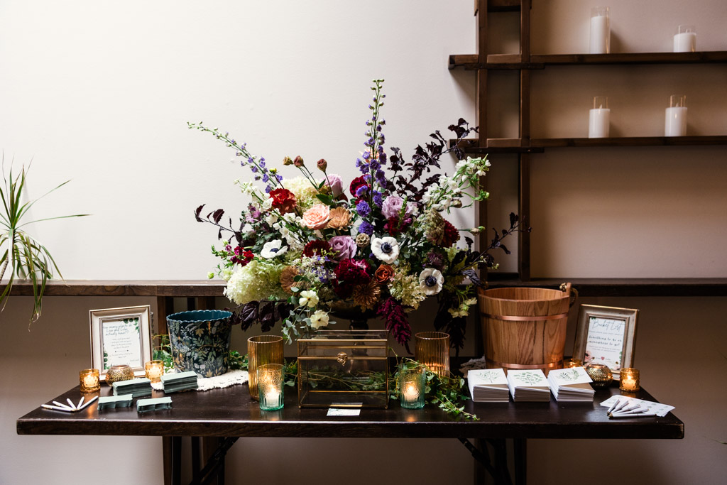 Card and gift table with a large floral arrangement, candles, framed signs, and stacked papers for Arbory Chicago wedding reception