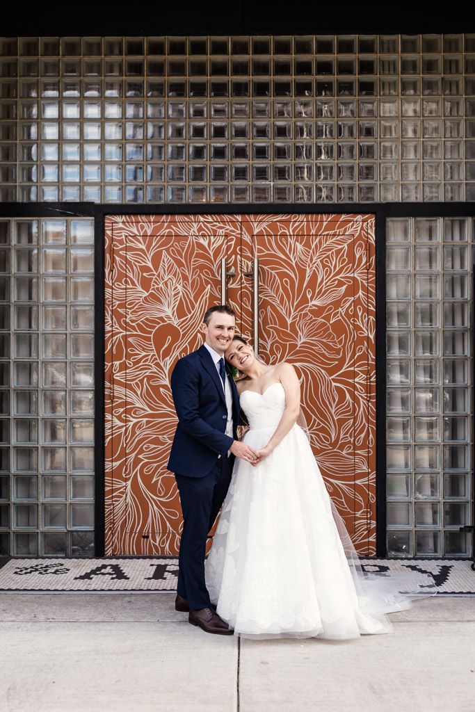 Portrait of bride and groom smiling and posing together in front of decorative doors with a floral pattern at The Arbory Chicago