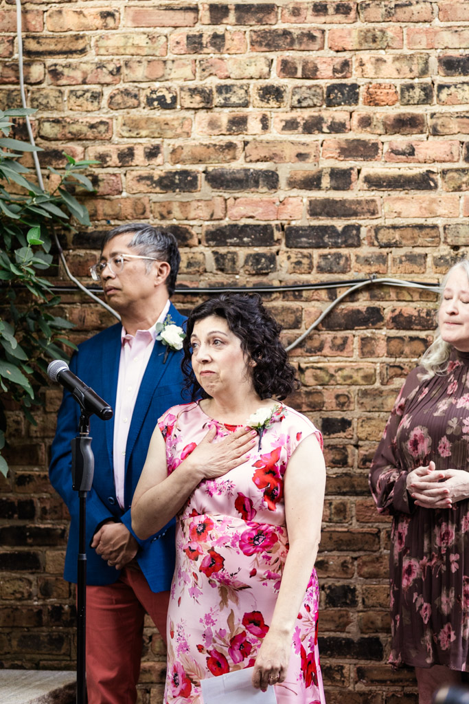 Three guests by a brick wall at Firehouse Chicago; the woman in front holds her hand to her chest, standing near a microphone