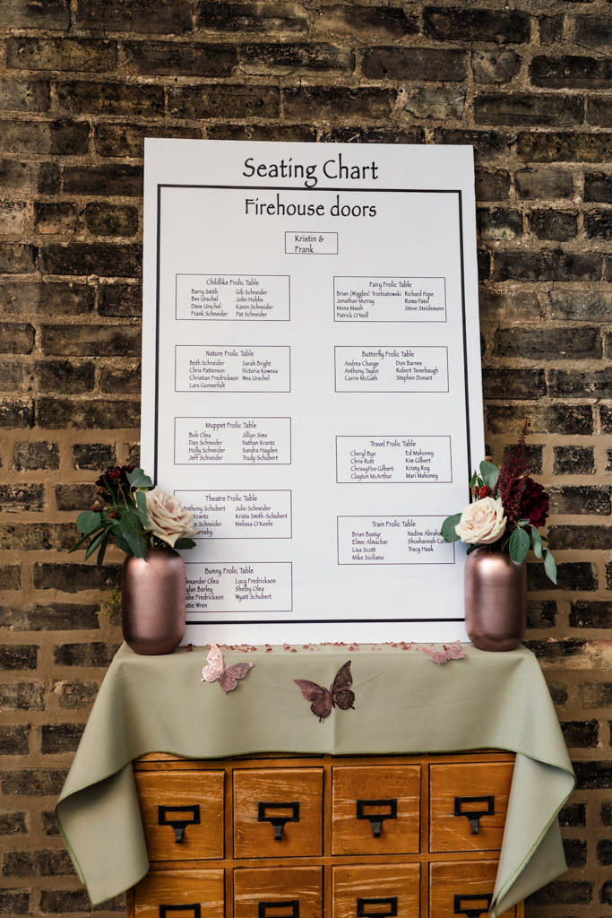 Seating chart on a brick wall above a green cloth-covered table with flowers and butterfly decorations for wedding reception at Firehouse Chicago