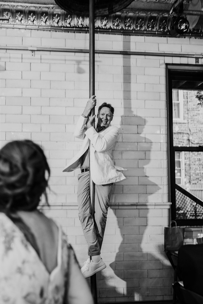 At Firehouse Chicago, a man in a suit playfully climbs a pole indoors while people watch, smiling.