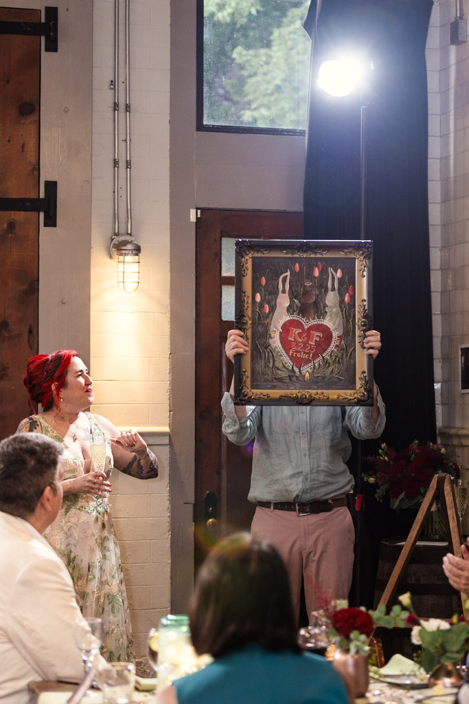 Groom holds up framed artwork during his wedding reception at Firehouse Chicago while guests look on