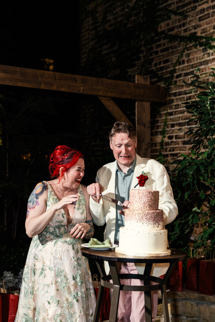 Bride and groom in wedding attire cut a tiered cake together during their outdoor wedding reception at Firehouse Chicago