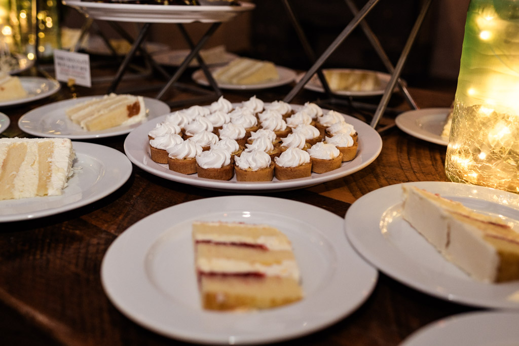 Plates of assorted cake slices and mini tarts with whipped cream arranged on a wooden table for wedding reception at Firehouse Chicago