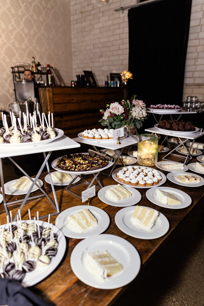 Dessert table at Firehouse Chicago with cake slices, cake pops, cookies, brownies, flowers, and a lit candle