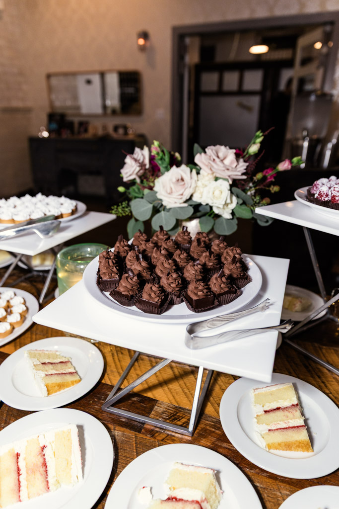 Chocolate cupcakes on a white tray, surrounded by floral decor and plates of layered cake slices for wedding reception at Firehouse Chicago