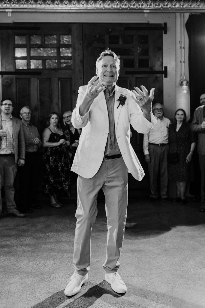 Black and white photo of groom in a light blazer on the dnace floor inside Firehouse Chicago while people watch and smile in the background