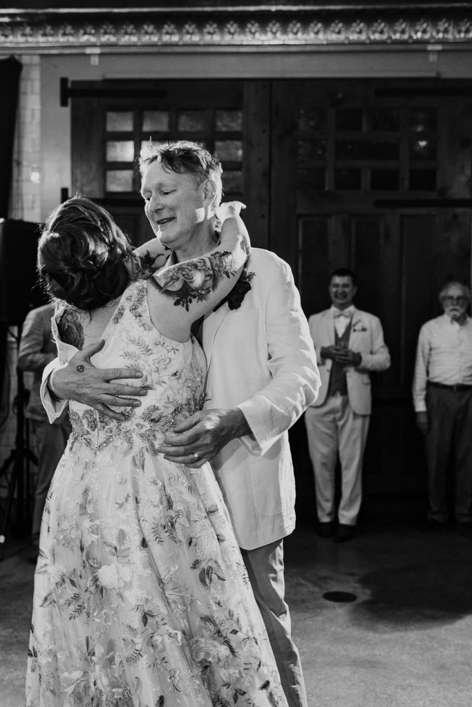 Black and white photo of bride and groom dancing together at their Firehouse Chicago wedding reception while others watch in the background