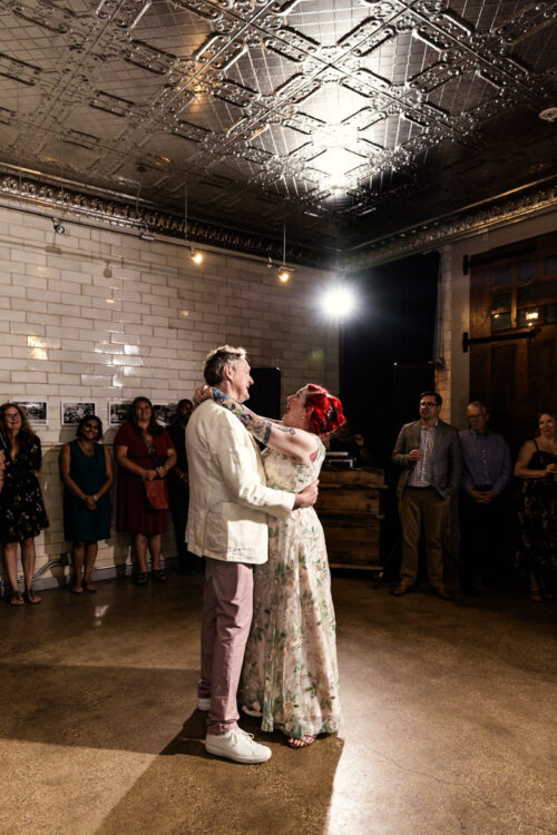 A couple shares a first dance at their wedding in the warmly lit Firehouse Chicago as guests stand and watch, creating an intimate and unforgettable moment.