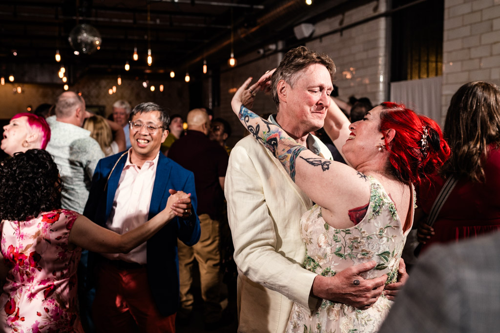 A joyful couple dances closely at a lively Firehouse Chicago party, surrounded by other smiling guests on the dance floor.
