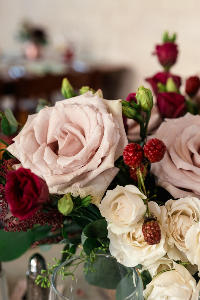 Detail photo of a floral arrangement at Firehouse Chicago, featuring pale pink roses, white roses, red berries, and lush greenery