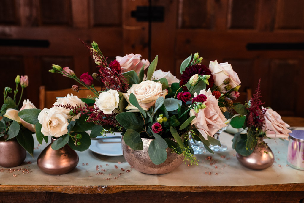 Floral centerpieces with pink and burgundy flowers in metallic vases on a rustic wooden table for Firehouse Chicago wedding celebration