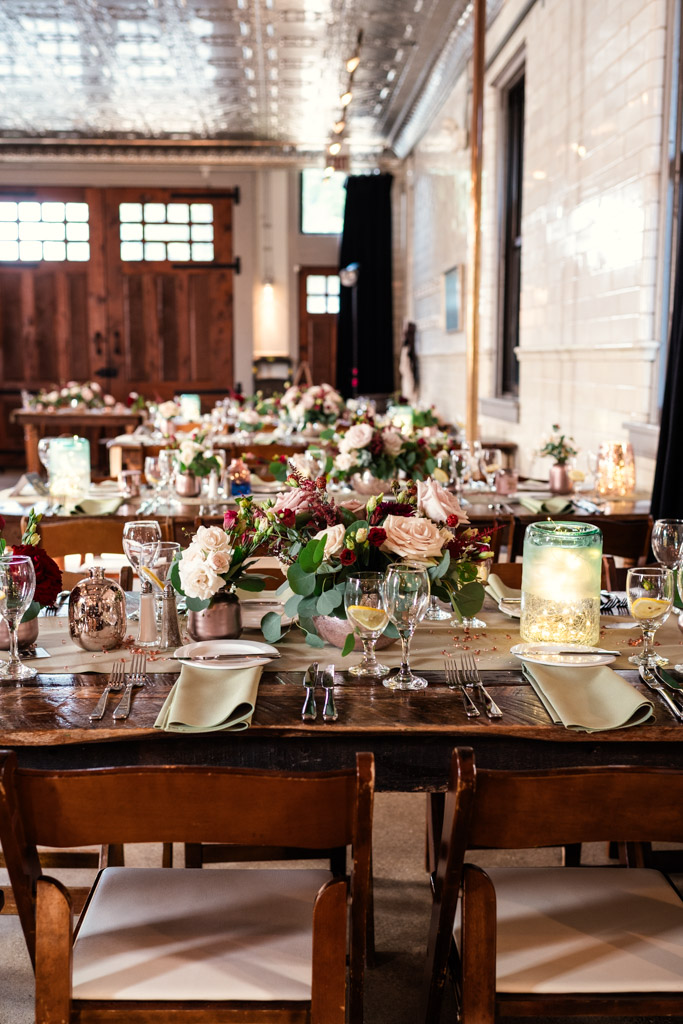 Rustic guest tables at Firehouse Chicago with floral centerpieces, candles, glassware, and plates set for summer wedding reception