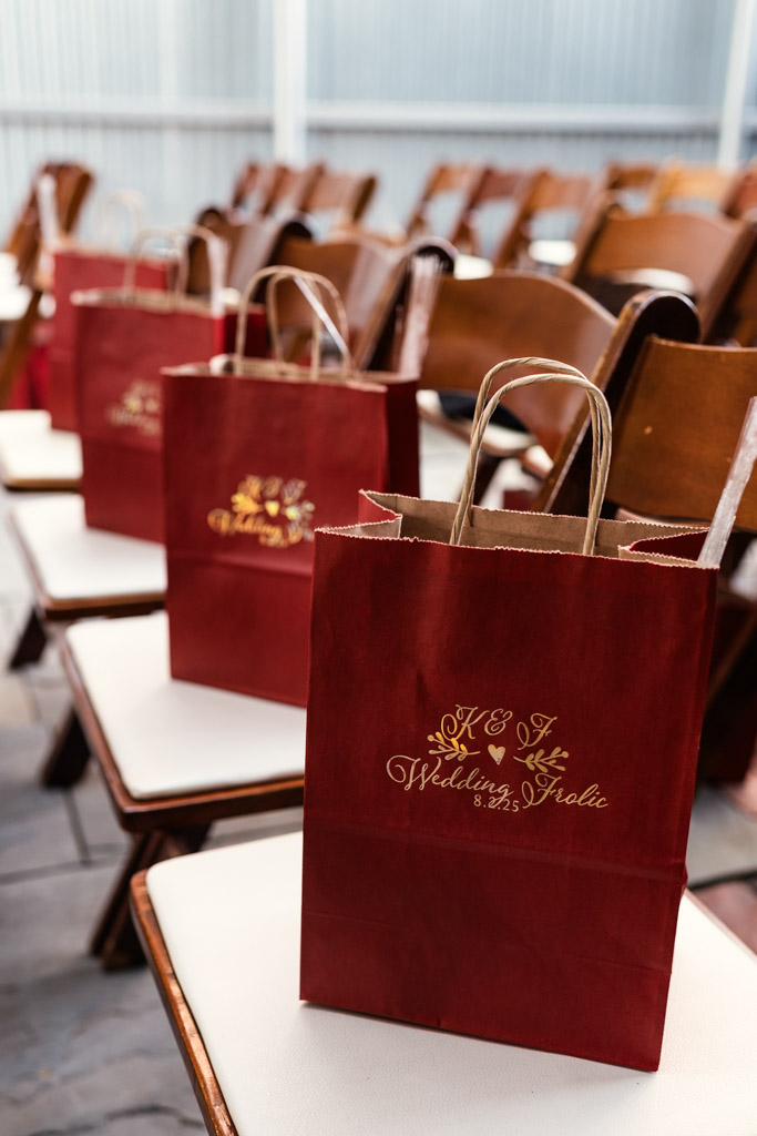 Red gift bags with gold lettering placed on white chairs for wedding at Firehouse Chicago