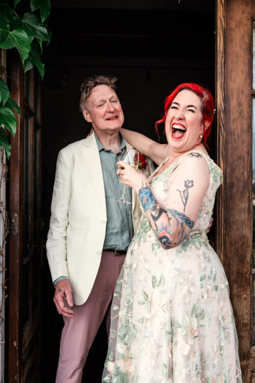 A joyful couple stands in the doorway of Firehouse Chicago, laughing together; the woman holds a drink and wears a floral dress.
