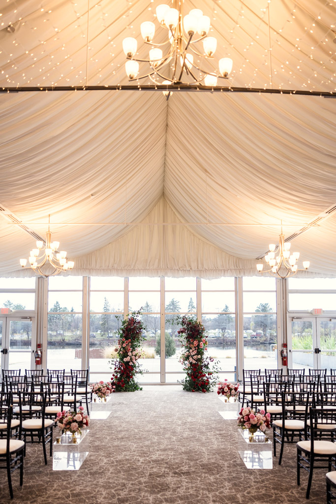Indoor wedding ceremony space at Marriott Lincolnshire with floral arrangements, black chairs, chandeliers, and a draped white ceiling.