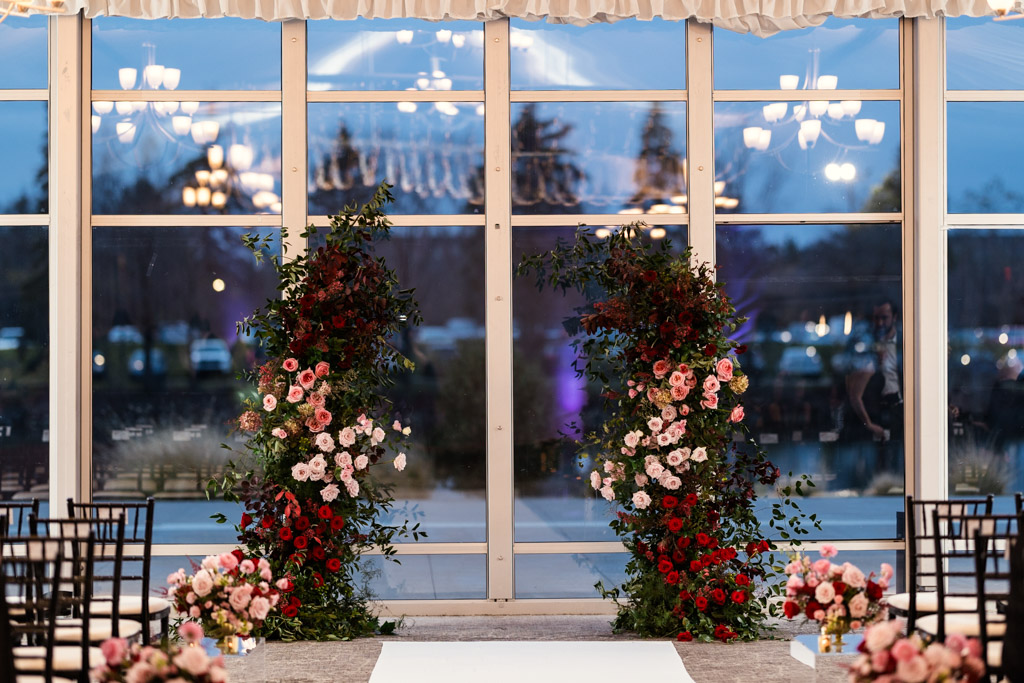 Indoor wedding ceremony space at Lincolnshire Marriott Resort, featuring floral arches of red and pink flowers, chairs, and a white aisle runner