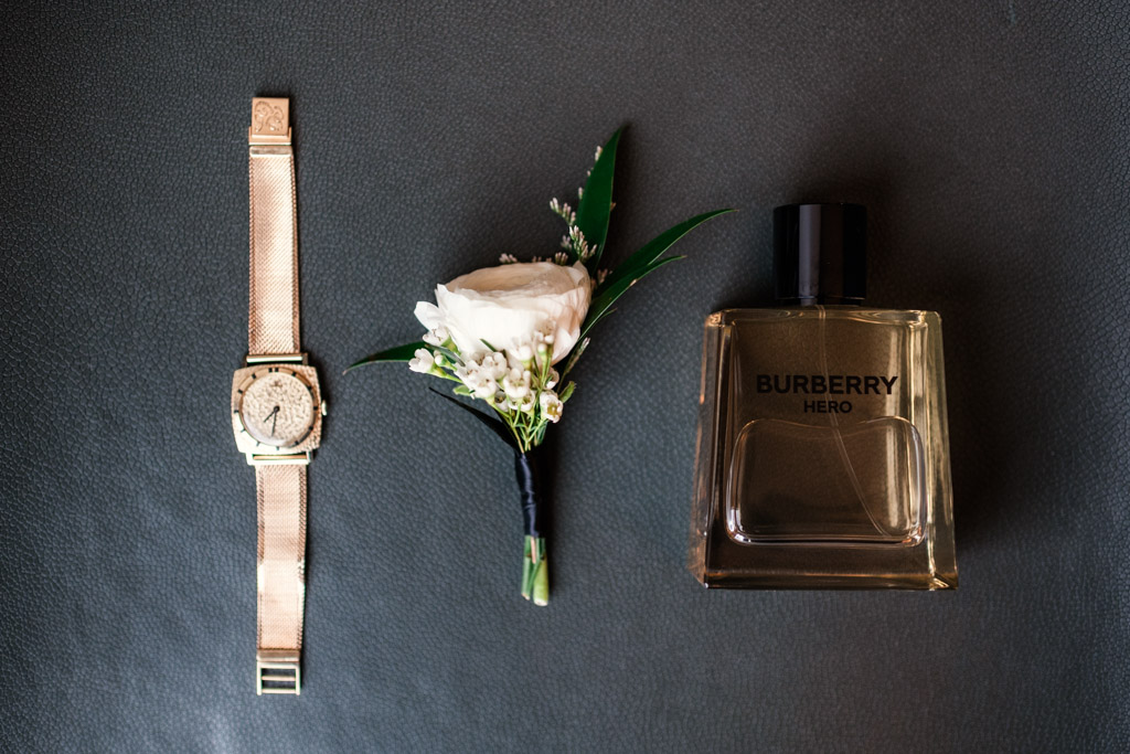Groom's gold wristwatch, white boutonniere, and a bottle of Burberry Hero cologne on a dark surface for Lincolnshire Marriott Resort wedding