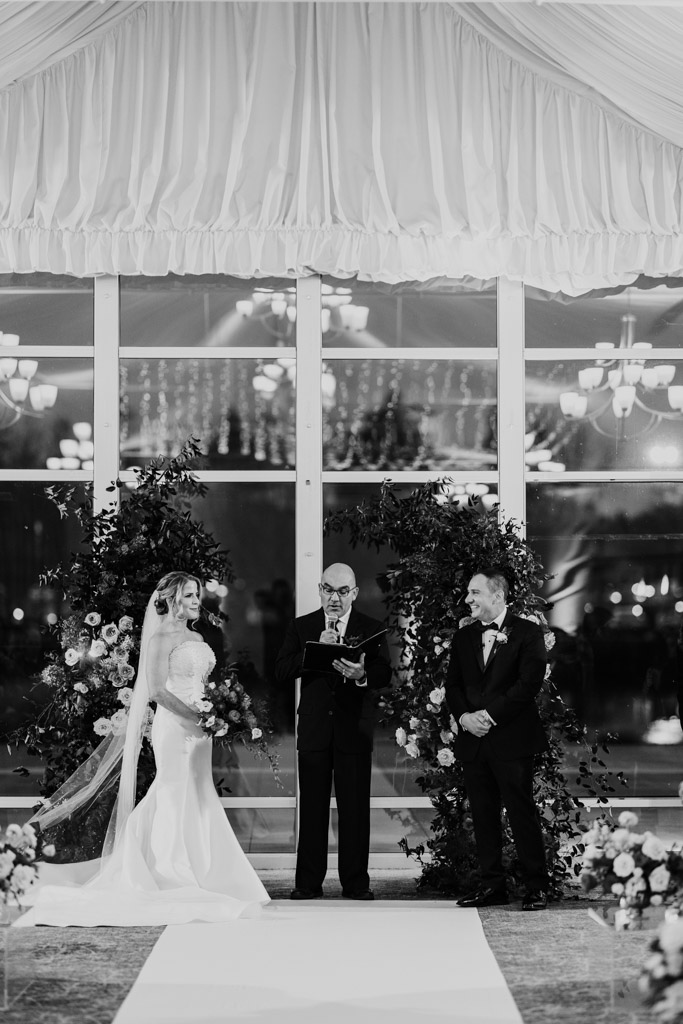Black and white photo of bride and groom standing with an officiant during their wedding ceremony at Lincolnshire Marriott Resort
