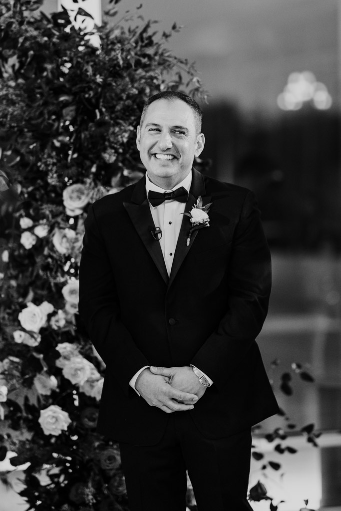 Black and white photo of smiling groom in a tuxedo standing by a floral arrangement during Lincolnshire Marriott Resort wedding ceremony