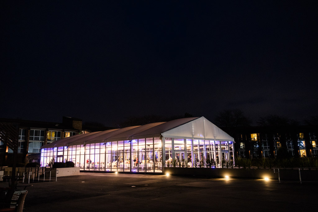 A large, glass-walled event tent wedding reception space at Lincolnshire Marriott Resort brightly lit at night, with people visible inside