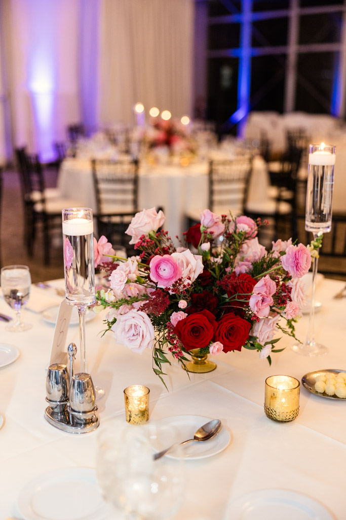 Guest table setting with pink and red flower centerpiece, candles, and glassware for wedding reception at Lincolnshire Marriott Resort