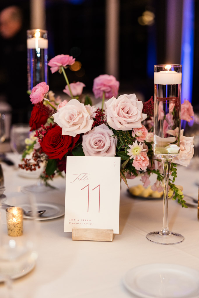 A floral centerpiece with roses, table number 11 card, and candles on a white tablecloth for wedding reception at Lincolnshire Marriott Resort