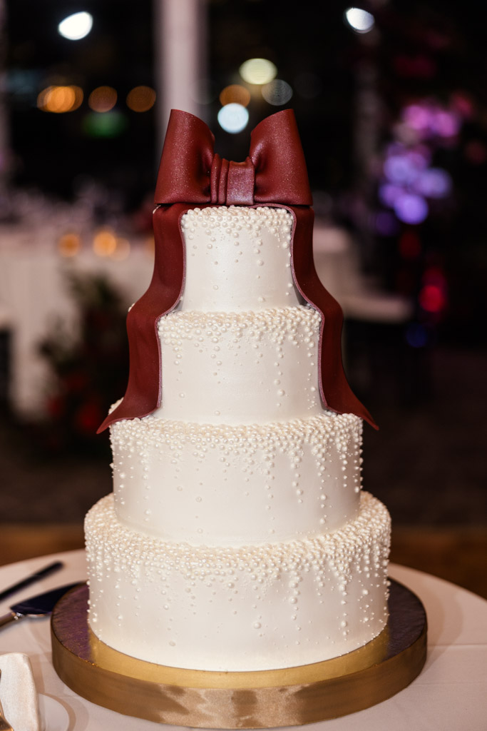Three-tier white cake with pearl-like decorations, topped with a large maroon fondant bow for Lincolnshire Marriott Resort wedding reception