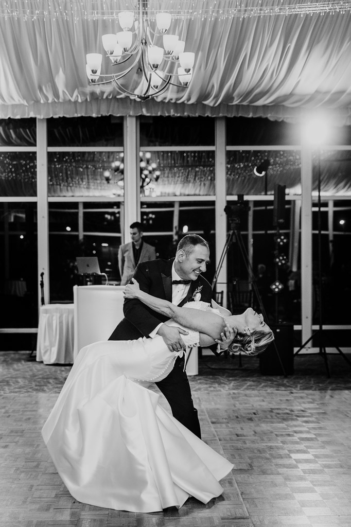 Black and white photo of newlyweds in formal attire dances as the groom dips the bride on a ballroom floor beneath chandelier lights during their wedding reception at Lincolnshire Marriott Resort