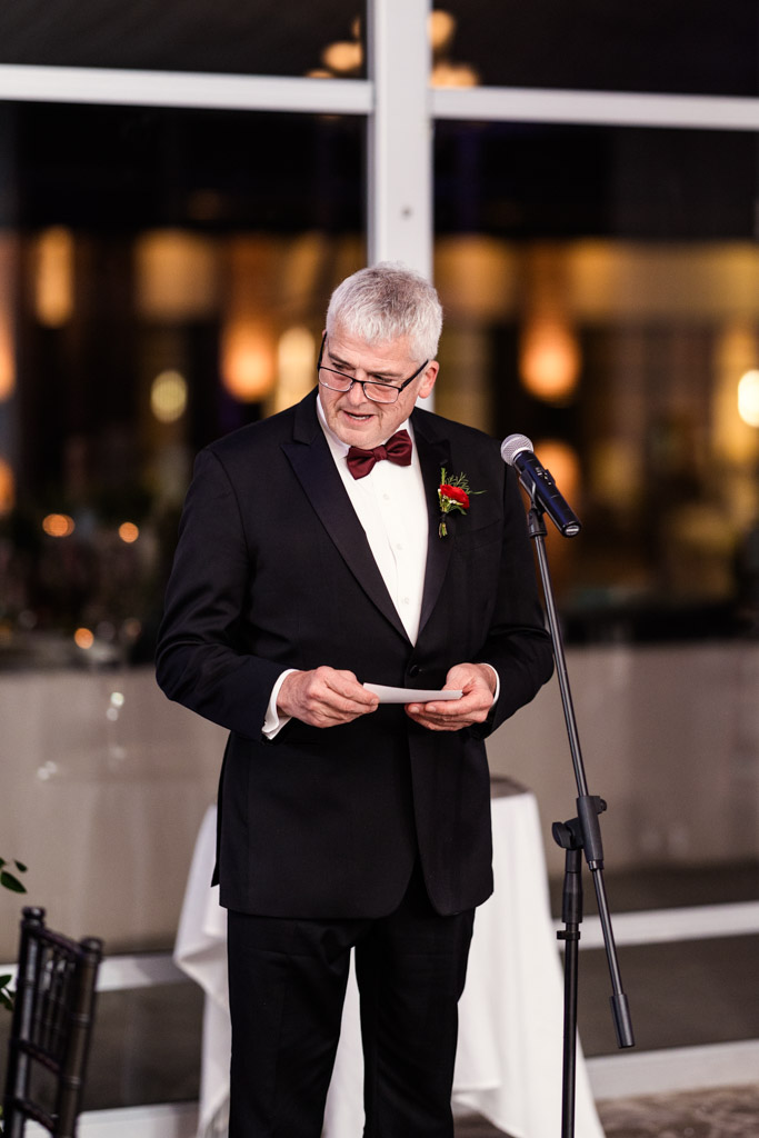 Bride's father in a tuxedo speaks at a microphone, holding notes, during Lincolnshire Marriott Resort wedding reception