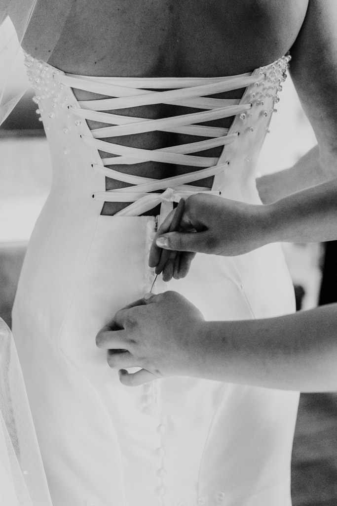 Black and white photo of hands fastening buttons on the back of a bride’s lace-up wedding dress before a Lincolnshire Marriott Resort wedding celebration