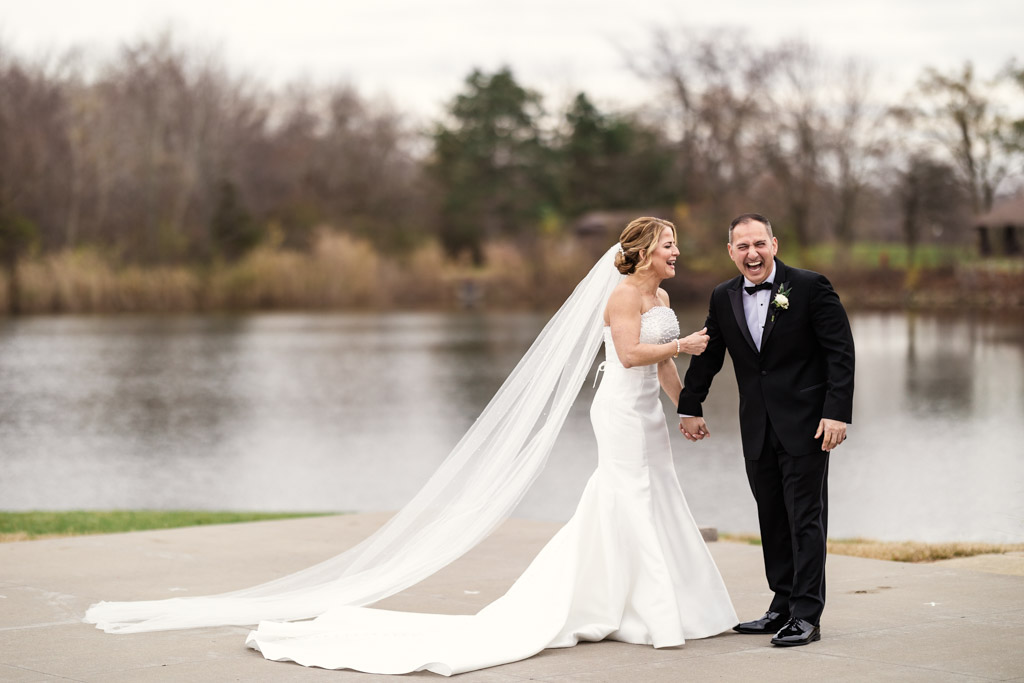 Candid photo of happy bride and groom laughing by a pond on a cloudy day before their Lincolnshire Marriott Resort wedding celebration