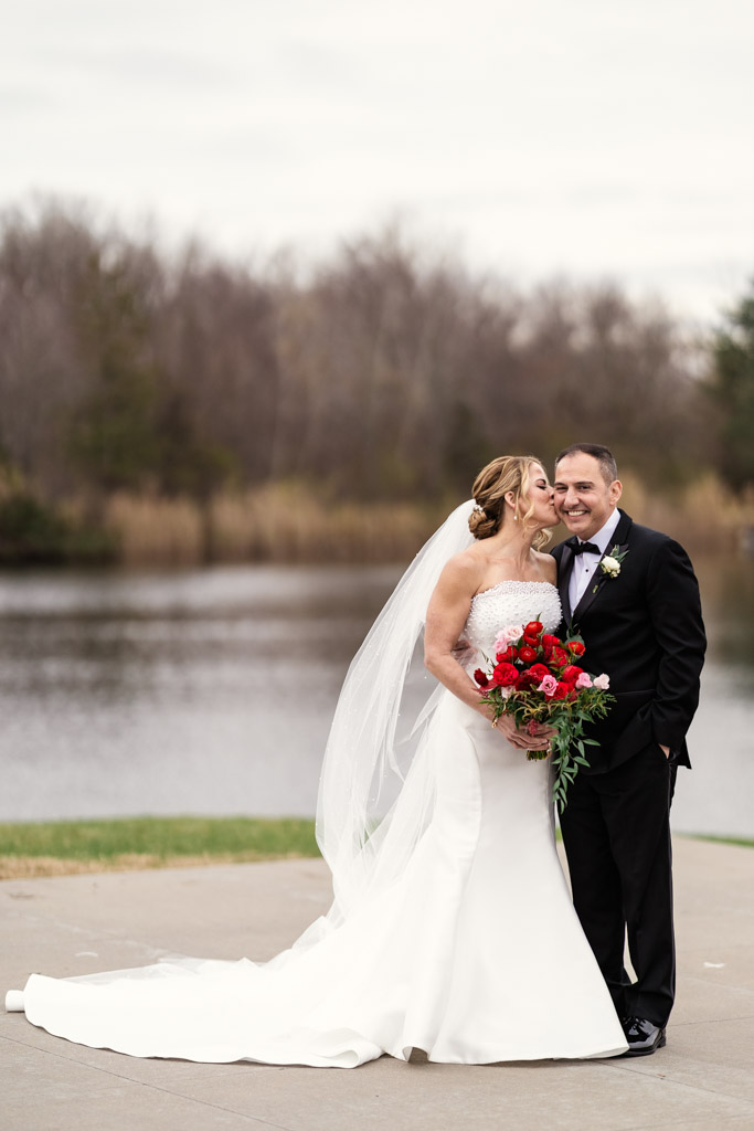 Bride in white gown kisses groom’s cheek by a pond at Lincolnshire Marriott Resort