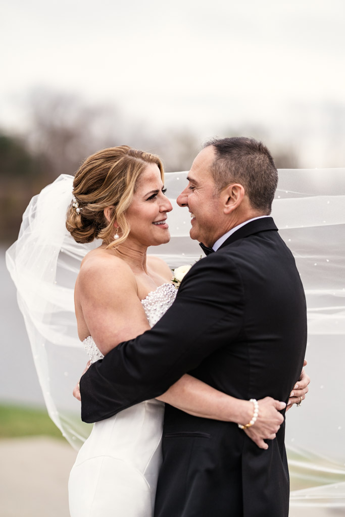 Bride and groom embrace outdoors at Lincolnshire Marriott Resort, smiling at each other, with bride's veil blowing in the wind behind them
