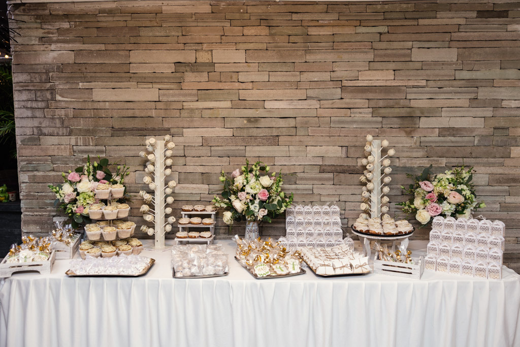 Dessert table with assorted sweets, cupcakes, and flower arrangements set against a stone wall at Mexico City wedding reception