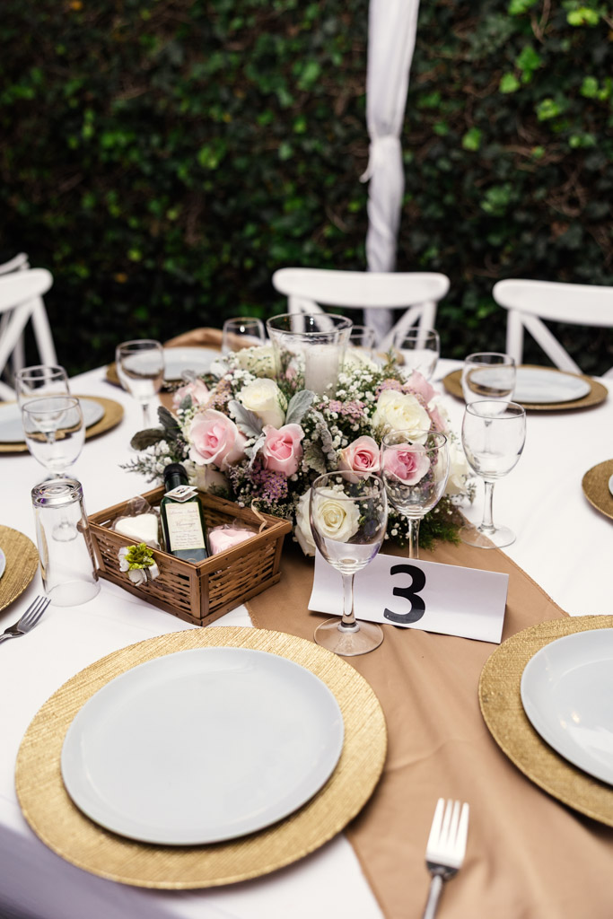 Guest table setting with white plates, gold chargers, pink flower centerpiece for Mexico City wedding reception