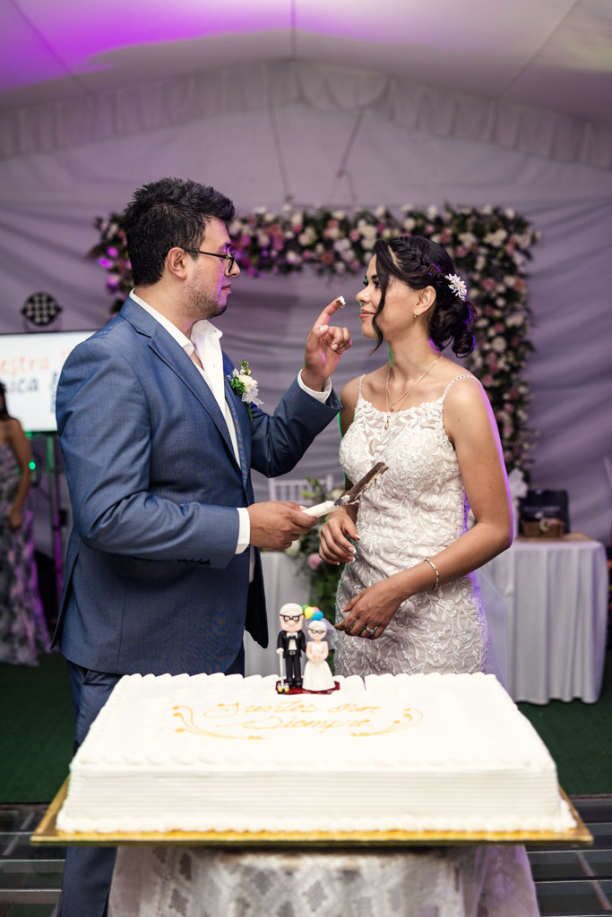 A groom in a blue suit gently touches the bride's nose as they stand by a wedding cake at their Mexico City wedding.