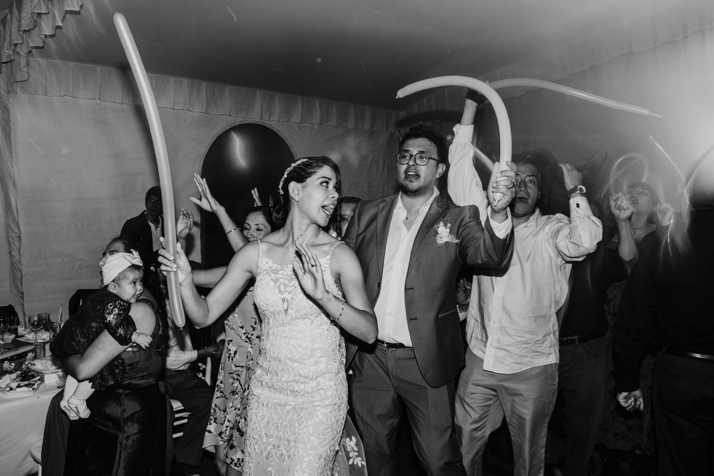 Black and white photo of bride and groom on the dance floor with guests holding long balloons during their Mexico City wedding reception